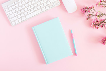 Office pink table, notepad, keyboard, flowers, notebook, stationery on pink background. Business minimal concept for women. Flat lay, top view, copy space
