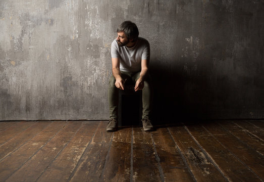 Thoughtful man sitting on chair against concrete wall