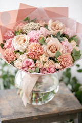 beautiful fresh cut bouquet of mixed flowers in vase on wooden table. The work of the florist at a flower shop. Delicate Pastel tones color