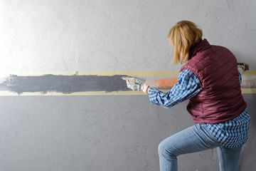 female painting a wall with masking tape and brush