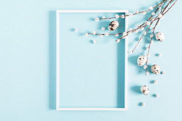 Easter holiday composition. Blank frame for text, easter eggs and willow branch on pastel blue background. Flat lay, top view, copy space
