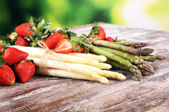 White and green asparagus with strawberries on wood