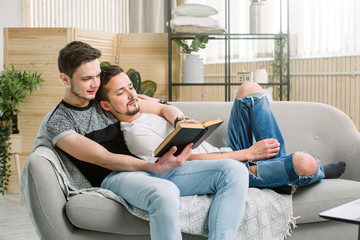 Obraz premium Attractive gay couple reading book on the sofa at home in living room