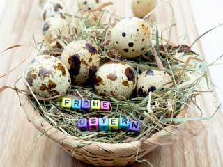 Obraz premium Wachteleier in einem kleinen Korb (Osternest) mit Text Frohe Ostern