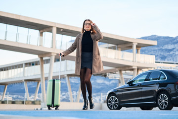 Young business woman walking against black luxury car on background.