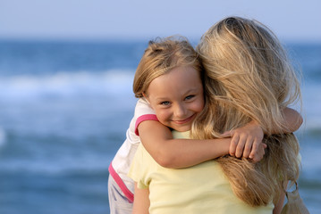 Fototapeta na wymiar Cute girl hugging her mom on the beach
