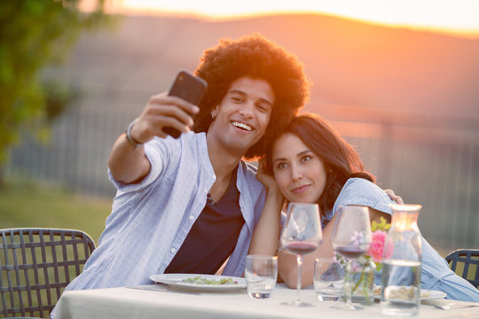 Smiling young couple taking selfie while sitting at table outdoors