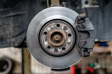 Front brake discs with caliper and brake pads in the car, on a car lift in a workshop.