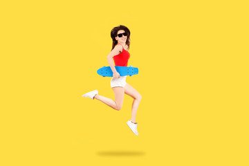 Fototapeta na wymiar Full length portrait of a girl in sunglasses with skateboard jumping on yellow background, youth summer concept