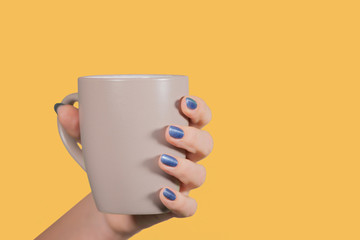 Closeup view of one beautiful female hand with painted blue glossy nails. Woman holding mug isolated on orange background. Horizontal color photography.