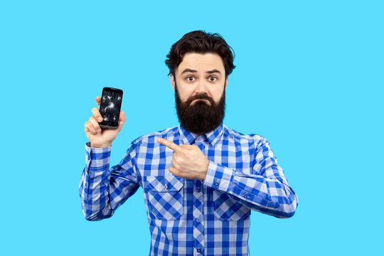 bearded sad hipster man pointing finger at broken smartphone screen, image on blue background, search concept gsm service