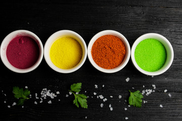 Multicolored bright seasonings on a wooden background, sea salt and greens