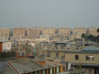 Fototapeta premium Genova, Italy - 04/02/2019: An amazing caption of the city of Genova from the hills in winter days, with a great grey sky, some tall skyscrapers and beautiful old buildings