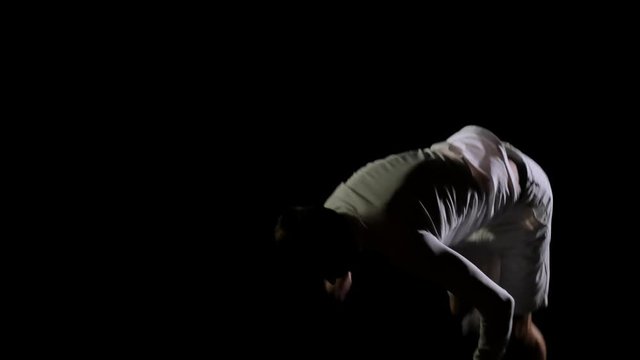 Athletic man in white clothes performs tricks jumping on a trampoline on a black monophonic background