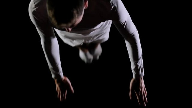Athletic man in white clothes performs tricks jumping on a trampoline on a black monophonic background