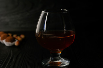 Cognac in a glass on a wooden dark background with truffles and hazelnuts