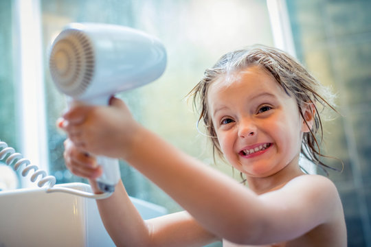 Blond girl drying her hair with hair dryer in bathroom