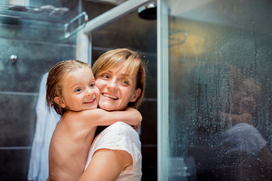 Smiling blond mother and daughter standing in bathroom