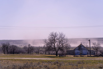 Fototapeta na wymiar Smoke from a fire on the plains of the river against a pinkish sky, a village house and a tree in the foreground