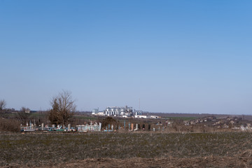 The cemetery on the side of the road in the foreground and the granary and grain elevator in the background during the day.