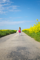 little child walking near rapeseed field under blue sky