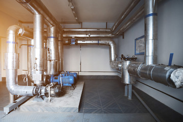 Pumps and pipes for water supply and steam installed in the boiler room. Blue toning with sunflare