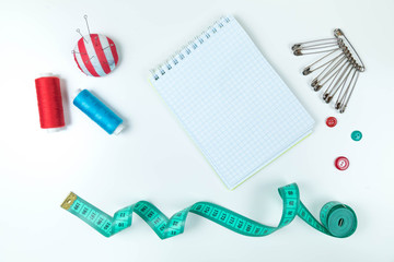 Sewing accessories: a centimetric measuring tape, threads, needles, a needle case, a notebook for records, buttons and pins. Top view