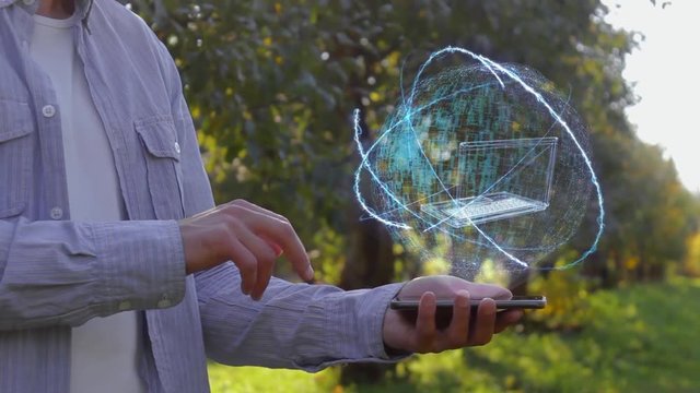 Unrecognizable man shows conceptual hologram with old laptop. Farmer on the background of the apple orchard in casual clothes with the technology of the future mobile screen