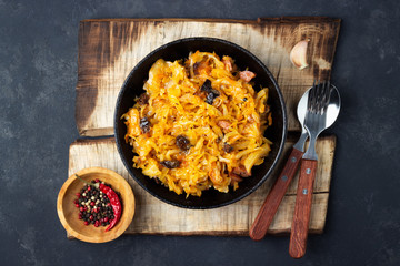Traditional dish of polish cuisine - Bigos from fresh cabbage, meat and prunes. Top view. Dark background.