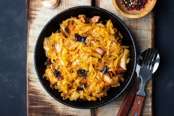 Traditional dish of polish cuisine - Bigos from fresh cabbage, meat and prunes. Top view. Dark background.