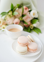 Elegant sweet dessert macarons, cup of coffee and pastel colored beige flowers bouquet
