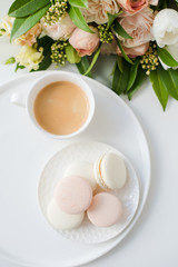 Elegant sweet dessert macarons, cup of coffee and pastel colored beige flowers bouquet