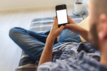Young man looking at smartphone screen sitting on sofa at home. Copy space.