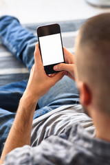 Young man looking at smartphone screen sitting on sofa at home. Copy space.