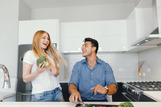 Man in a kitchen. A handsome man with woman at home. Male and famale at home with vagatables. Blonde with handsome guy prepare salad