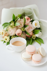 Elegant sweet dessert macarons, cup of coffee and pastel colored beige flowers bouquet