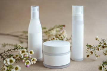 Set of  white cosmetic jars two tall bottles and one round  bottle on beige background decorated with flowers