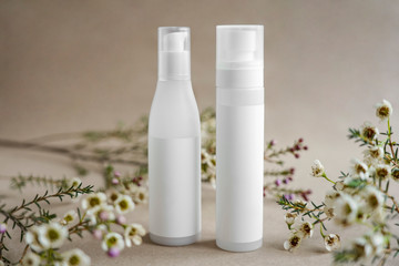 Obraz na płótnie Canvas Two white cosmetic bottles on a beige background decorated with flowers