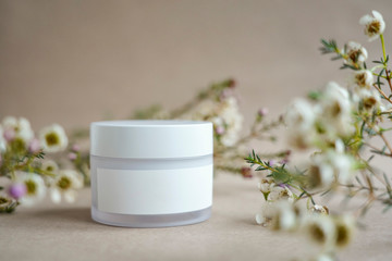 Fototapeta na wymiar White round cosmetic jar on a beige background decorated with white flowers