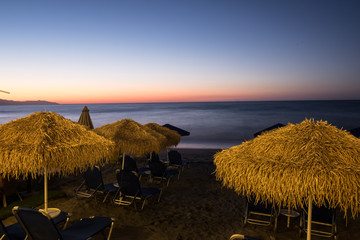 Tropical beach in sunset with beach chairs and umbrella.​