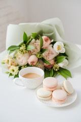 Elegant sweet dessert macarons, cup of coffee and pastel colored beige flowers bouquet