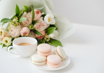 Elegant sweet dessert macarons, cup of coffee and pastel colored beige flowers bouquet