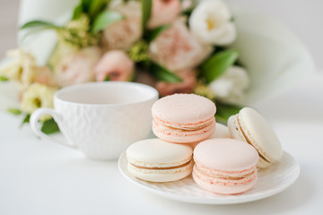 Fototapeta na wymiar Elegant sweet dessert macarons, cup of coffee and pastel colored beige flowers bouquet