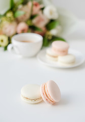Elegant sweet dessert macarons, cup of coffee and pastel colored beige flowers bouquet