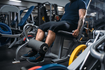 Fototapeta na wymiar Male person trains legs on exercise machine in gym