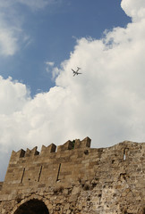 Plane flying over the Rhodes Old Town, Greece / Castle wall / on a sunny day with clouds and blue sky on the background /  aircraft, airplane / traveling concept Unesco world heritage sight 