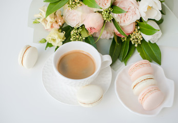 Elegant sweet dessert macarons, cup of coffee and pastel colored beige flowers bouquet