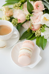 Elegant sweet dessert macarons, cup of coffee and pastel colored beige flowers bouquet