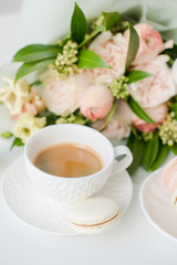 Fototapeta na wymiar Elegant sweet dessert macarons, cup of coffee and pastel colored beige flowers bouquet