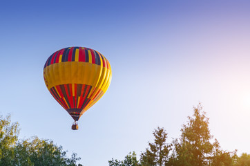Fototapeta na wymiar Colorful hot air balloon is flying in the blue sky above the trees